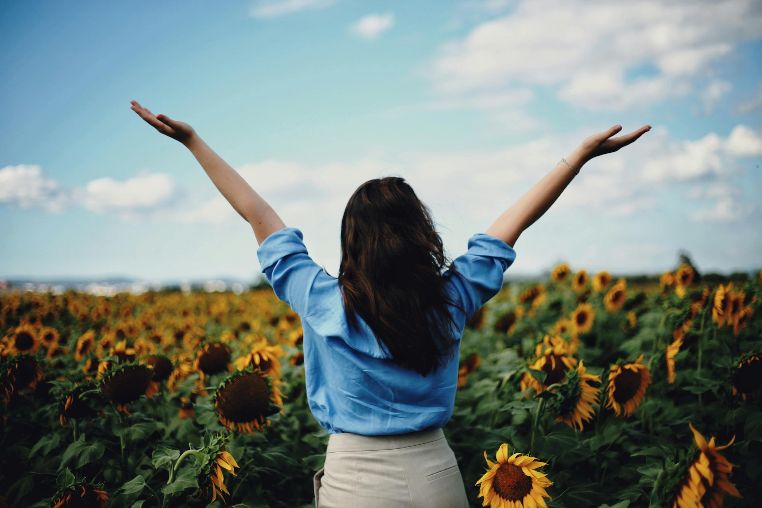 A woman joyously raises her arms surrounded by a vibrant sunflower field in İzmir, Türkiye.