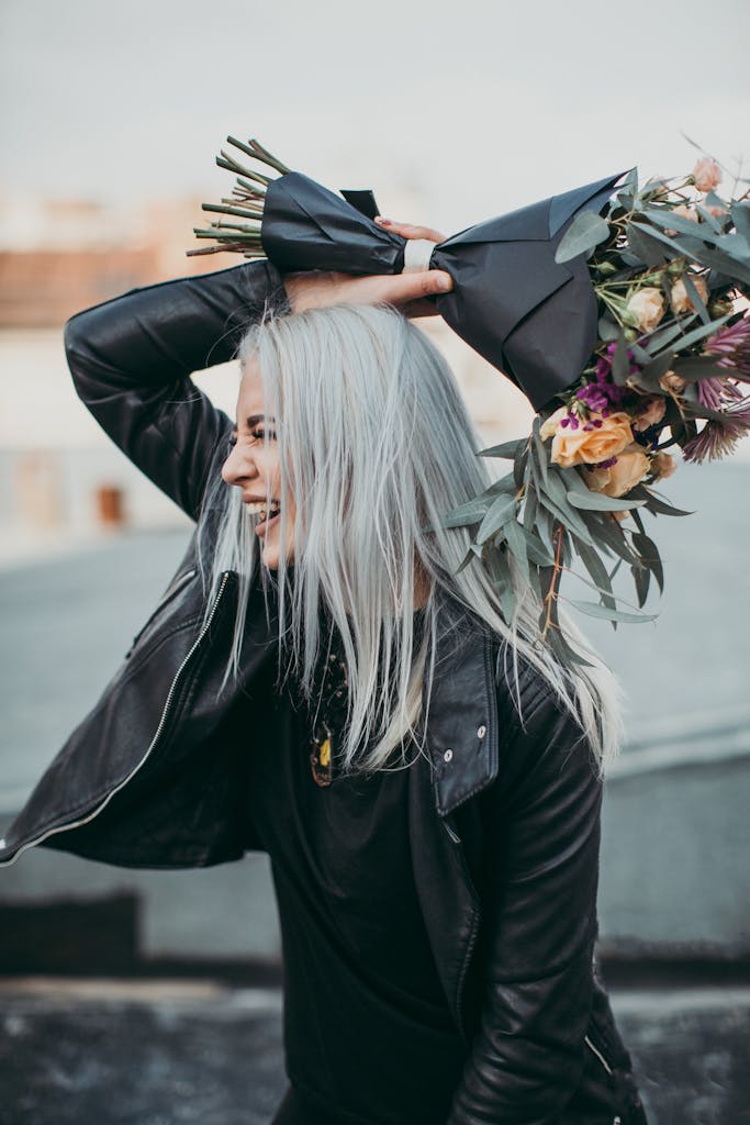 Fashionable woman in leather jacket holding flowers, feeling joyful outdoors.